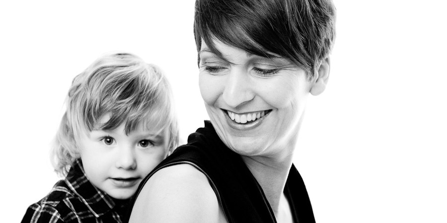 Family photography picture of Mum sitting side-on smiling with toddler boy seated behind her